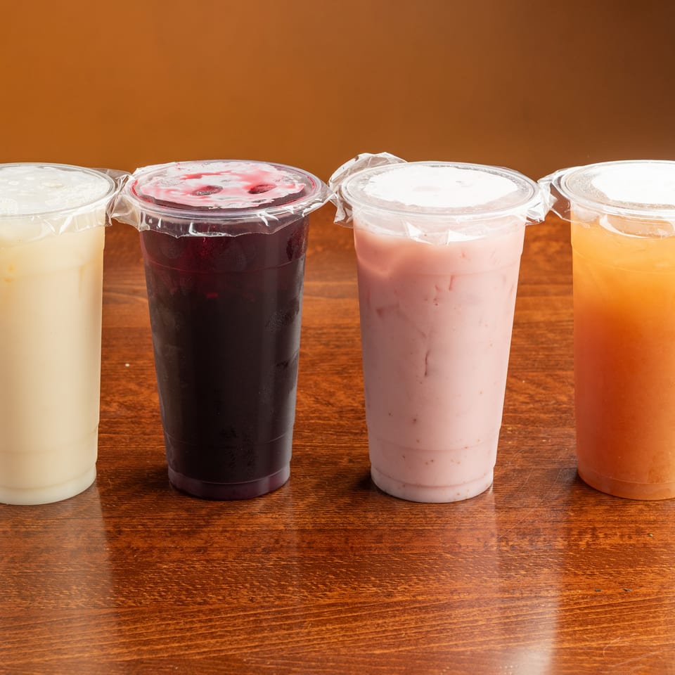 Four plastic cups of colorful bubble tea drinks, including white, purple, pink, and orange.