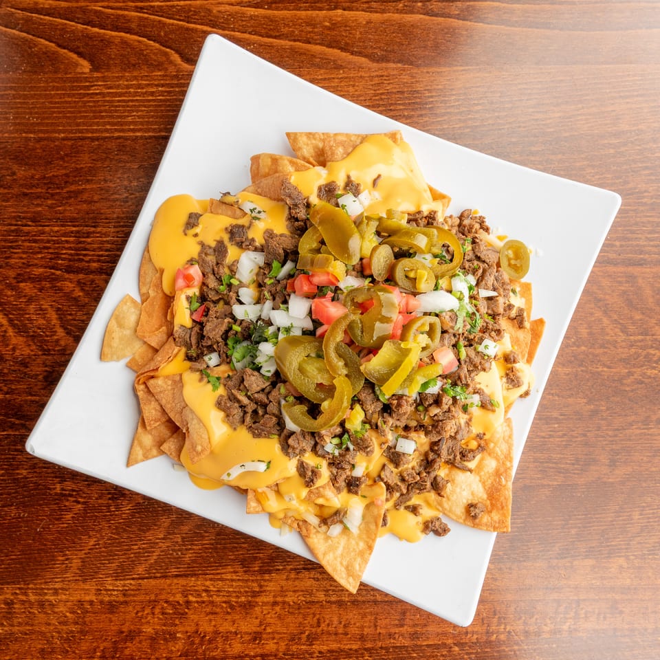 Loaded nachos with melted cheese, ground beef, diced tomatoes, onions, and jalapeños on a white plate.