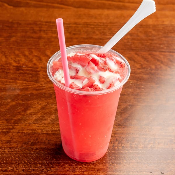Strawberry smoothie with condensed milk and fresh strawberry chunks, with a pink straw and white spoon.