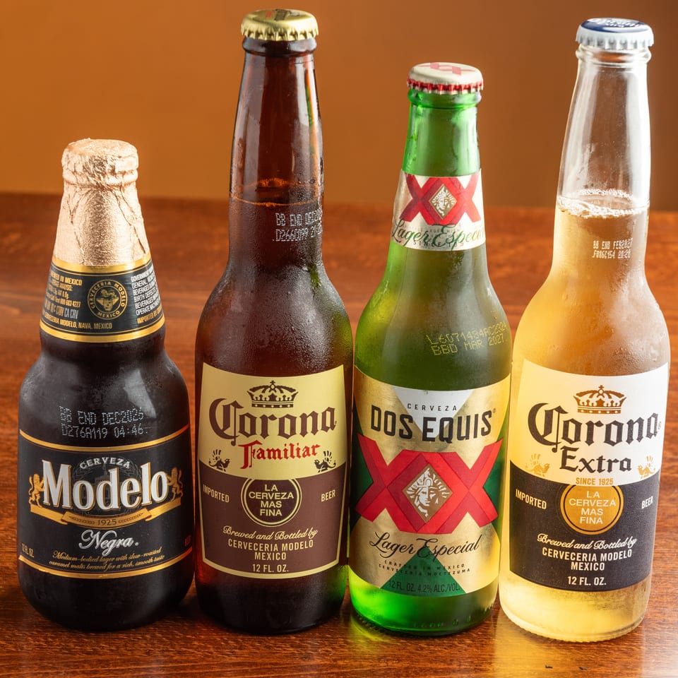 Four cold Mexican beer bottles, including Modelo Negra, Corona Familiar, Dos Equis, and Corona Extra.
