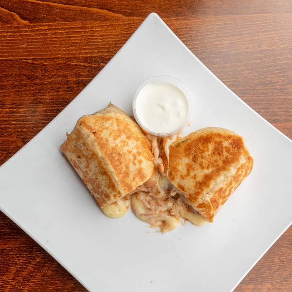 Two golden-brown quesadilla halves with melted cheese and filling, served with a side of sour cream.
