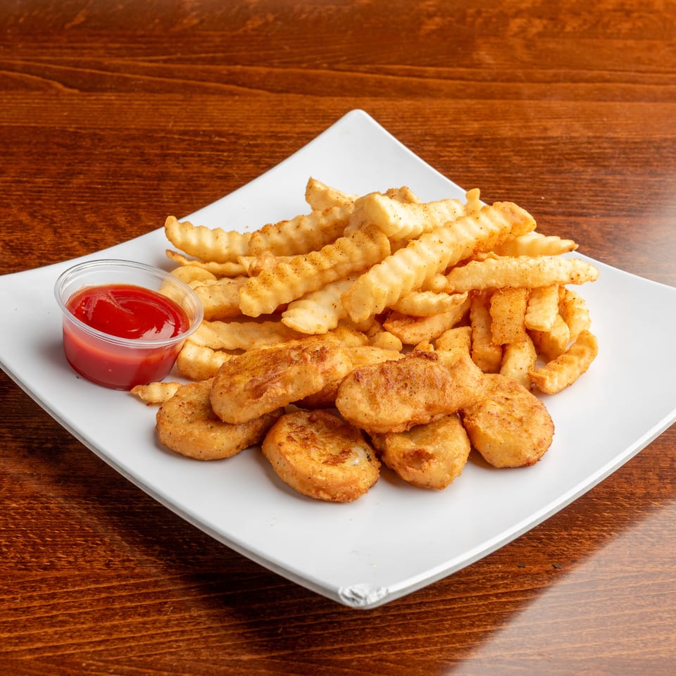 A white plate holds crispy chicken nuggets, crinkle-cut fries, and a small cup of ketchup on a wooden table.