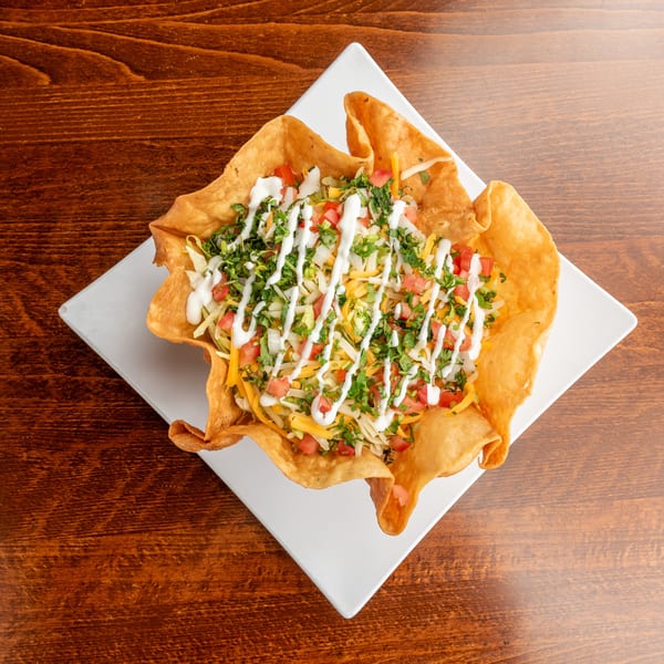 Taco salad in a crispy fried tortilla bowl, topped with sour cream, on a white plate.
