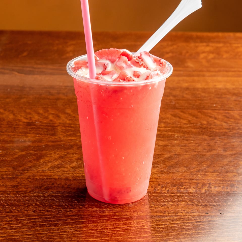 Strawberry smoothie with cream and fresh strawberries, served with a pink straw and spoon.