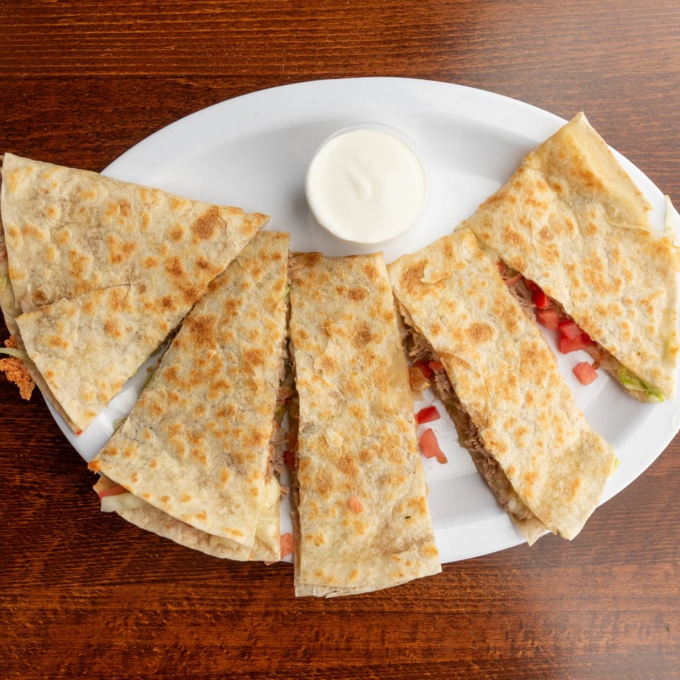 A white platter of quesadilla slices filled with meat, cheese, and vegetables, with a side of sour cream.